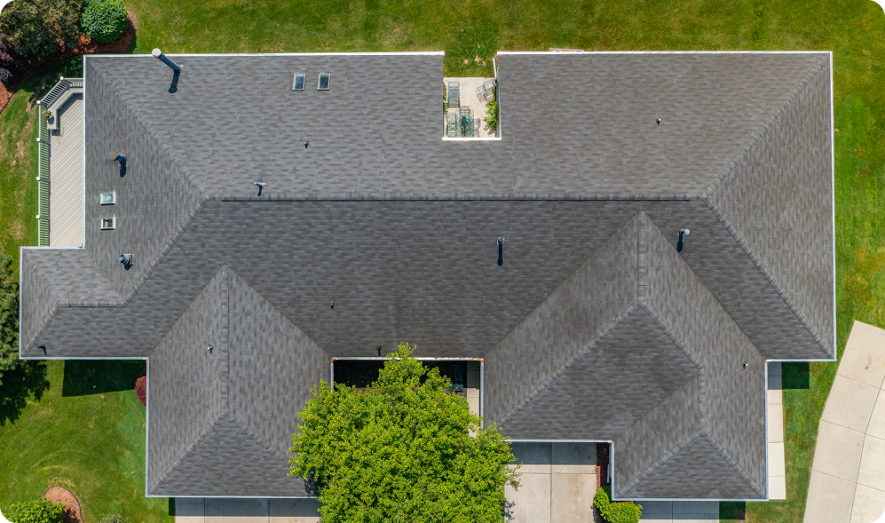 Aerial view of a house with a dark gray shingled roof, surrounded by green grass and trees in St Louis, featuring a driveway and deck—perfect for STL Roof Renew’s expert Roof Rejuvenation services.